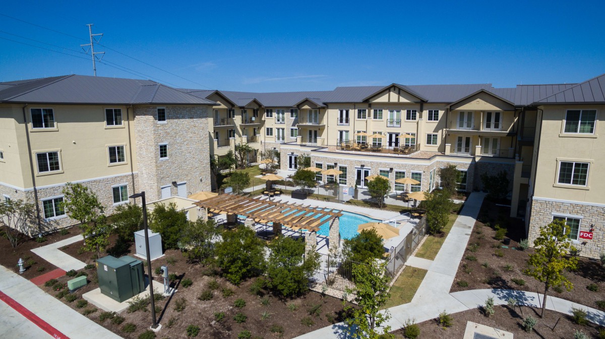 Aerial view of a modern apartment complex with a central swimming pool and landscaped gardens.