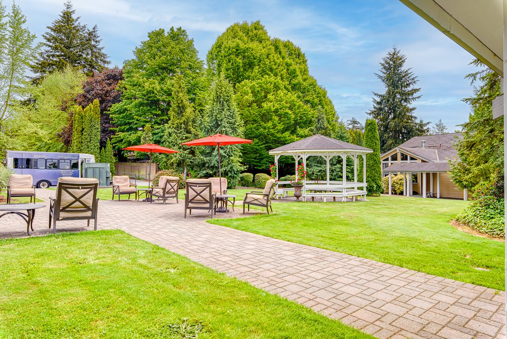 A serene garden scene with a gazebo, patio furniture, and umbrellas on a sunny day.