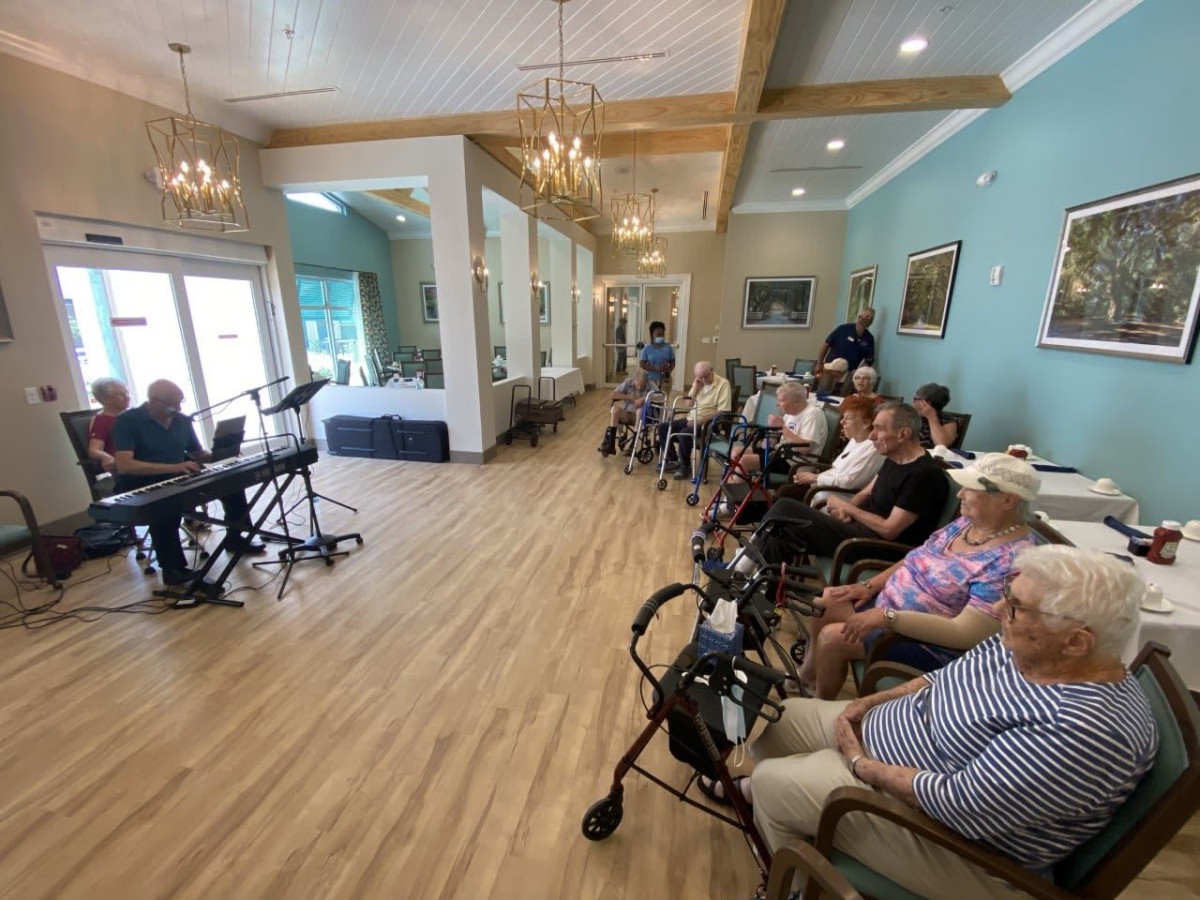 A group of elderly people enjoying a piano performance in a spacious community room.