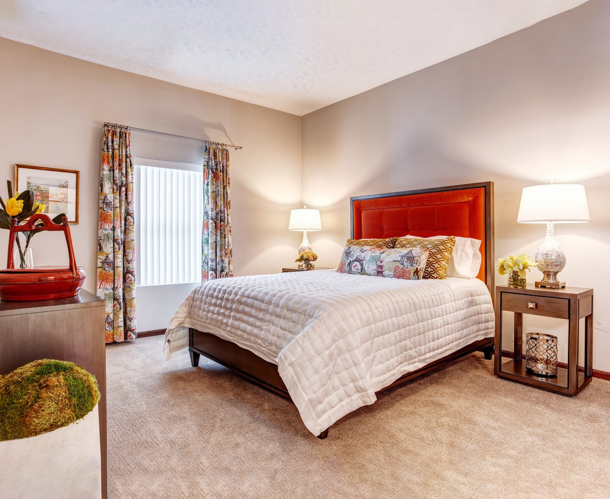 A cozy bedroom with a large bed, two bedside lamps, and patterned curtains creating a warm atmosphere.
