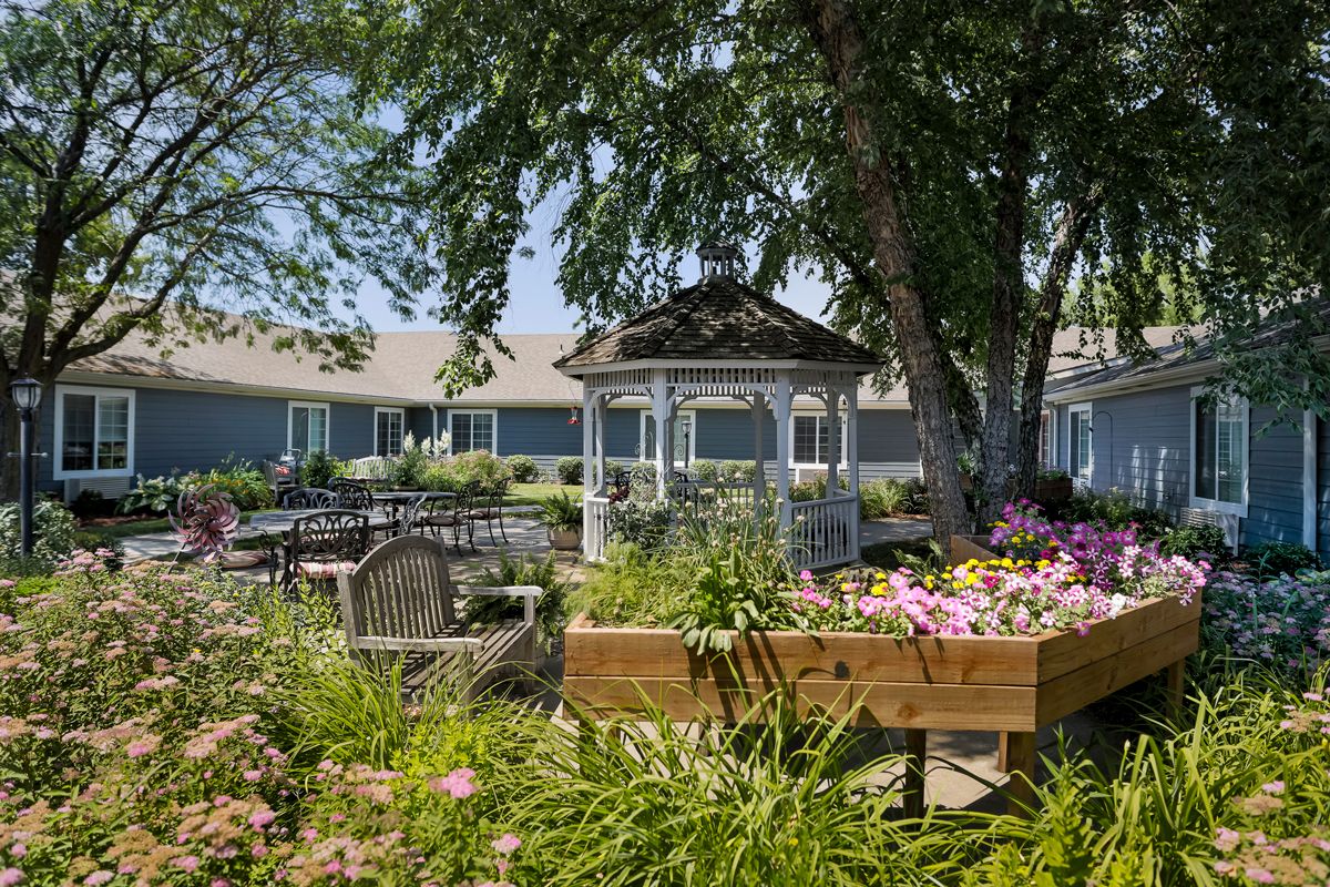 A peaceful garden with a gazebo and vibrant flowers under the shade of trees.