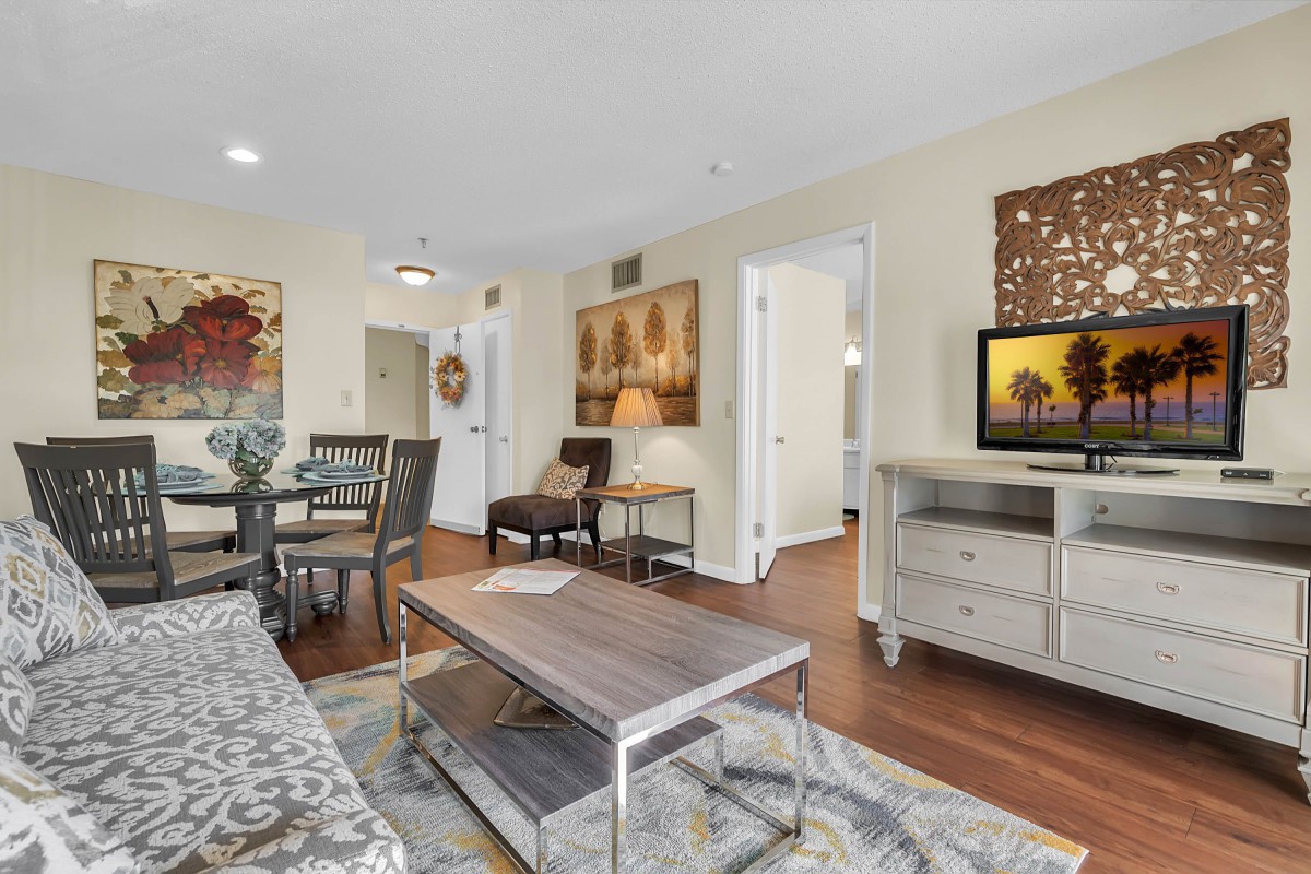 A stylishly decorated living room featuring a coffee table, dining area, and TV with artwork on the walls.
