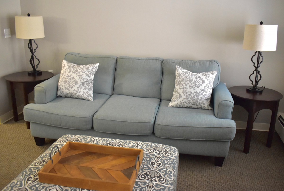A comfortable gray sofa with patterned pillows in a living room setting, accompanied by a wooden tray on an ottoman.