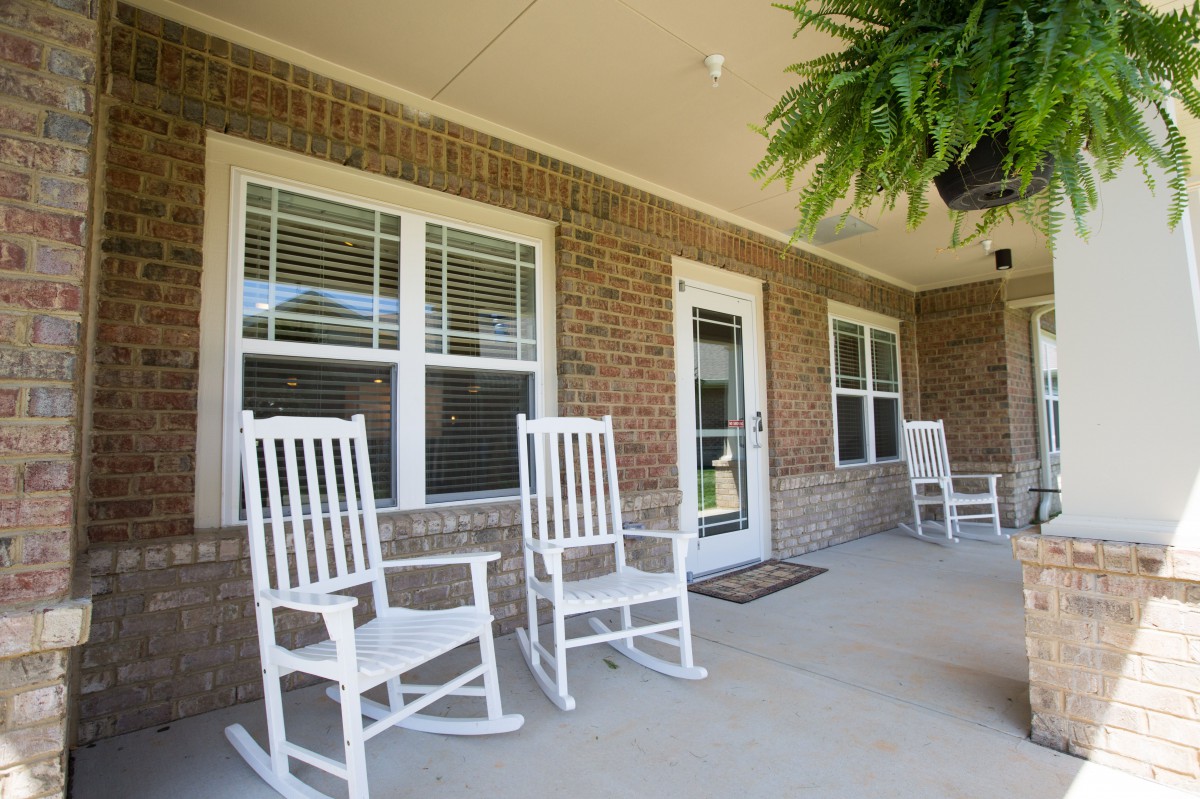 A cozy porch with white rocking chairs and potted fern, set against a brick wall.
