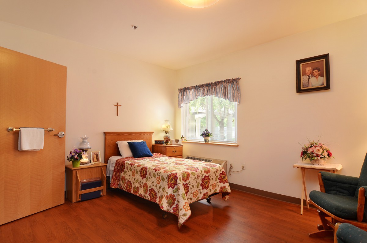 A cozy bedroom with a single bed, decorated with a floral cover and a bedside table with a lamp.