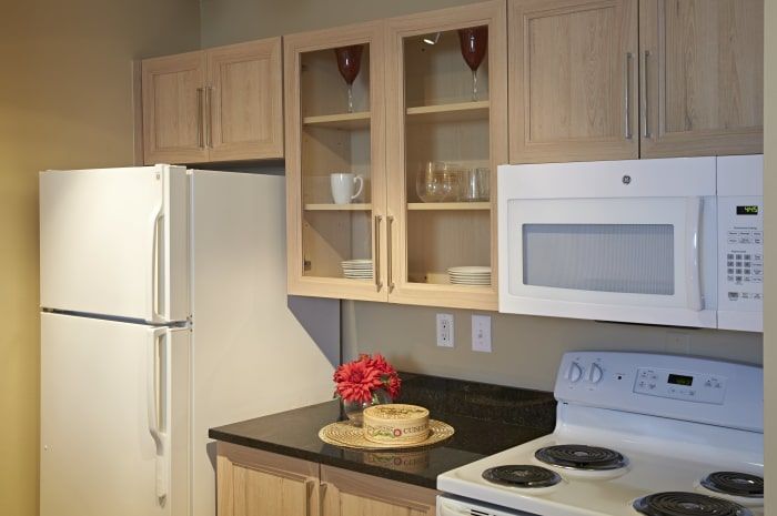 A modern kitchen with wooden cabinets, a white refrigerator, microwave, stove, and a decorated countertop.