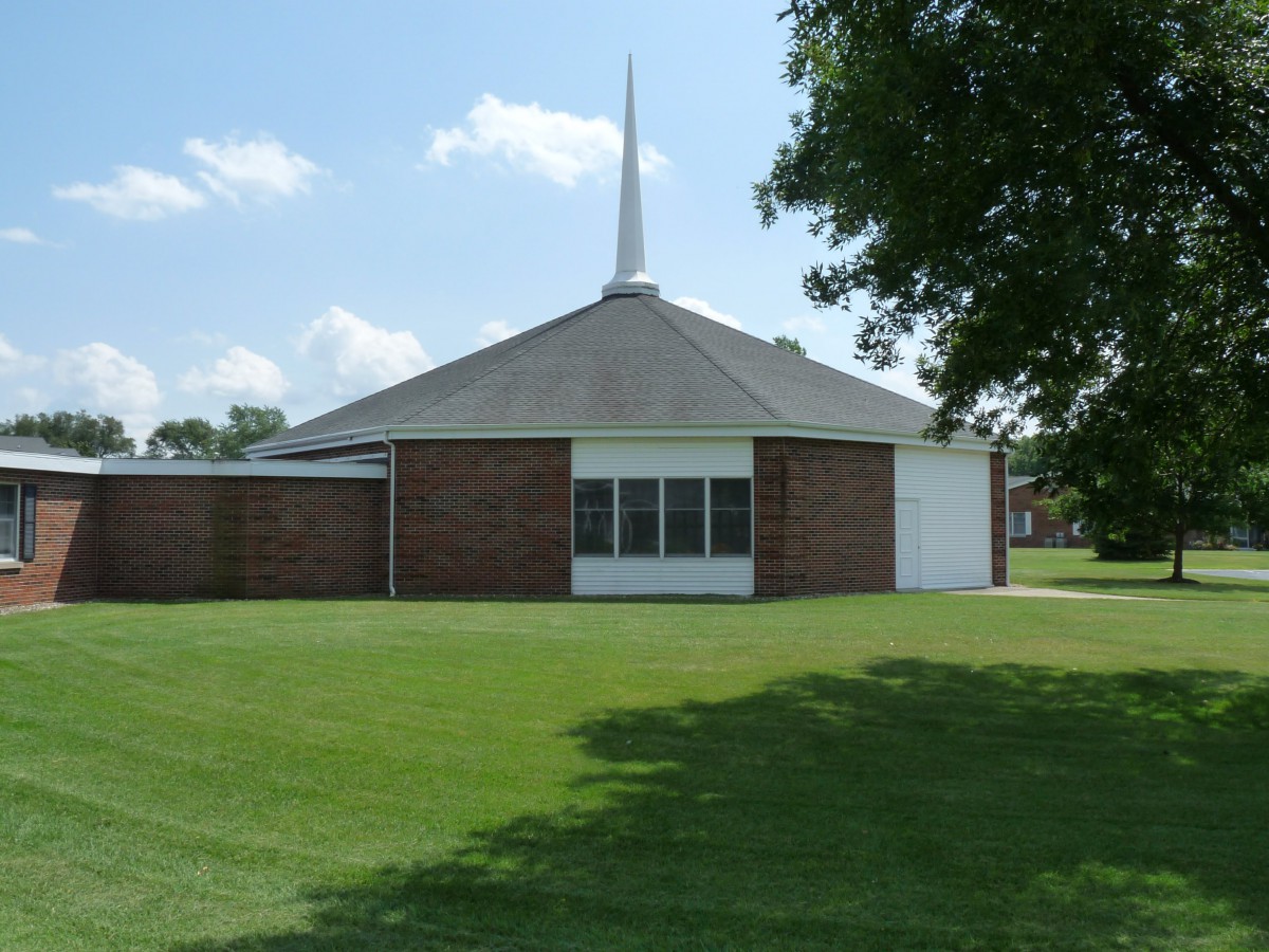 A brick church with a steeple set against a clear blue sky and surrounded by a green lawn.