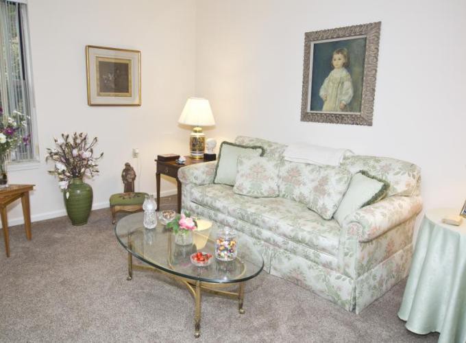 A cozy living room with a floral-patterned sofa, glass coffee table, and elegant artwork on the walls.