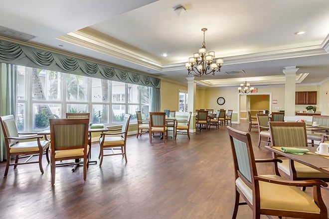 A spacious dining area with elegant chandeliers, wooden flooring, and large windows allowing natural light.