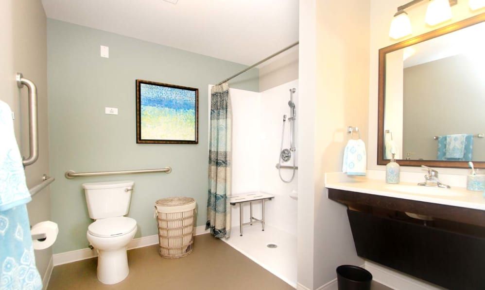 A modern bathroom featuring a shower with a bench, toilet, and sink, complemented by wall art and neutral tones.
