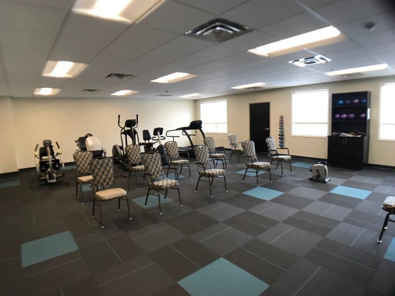 A fitness room with various exercise equipment and chairs arranged in rows.