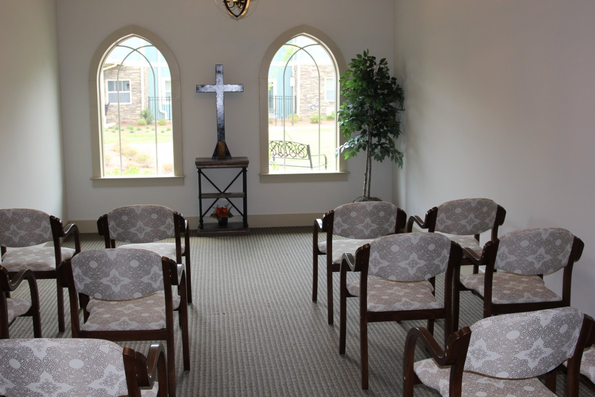 A small chapel with rows of chairs facing a cross and two arched windows.