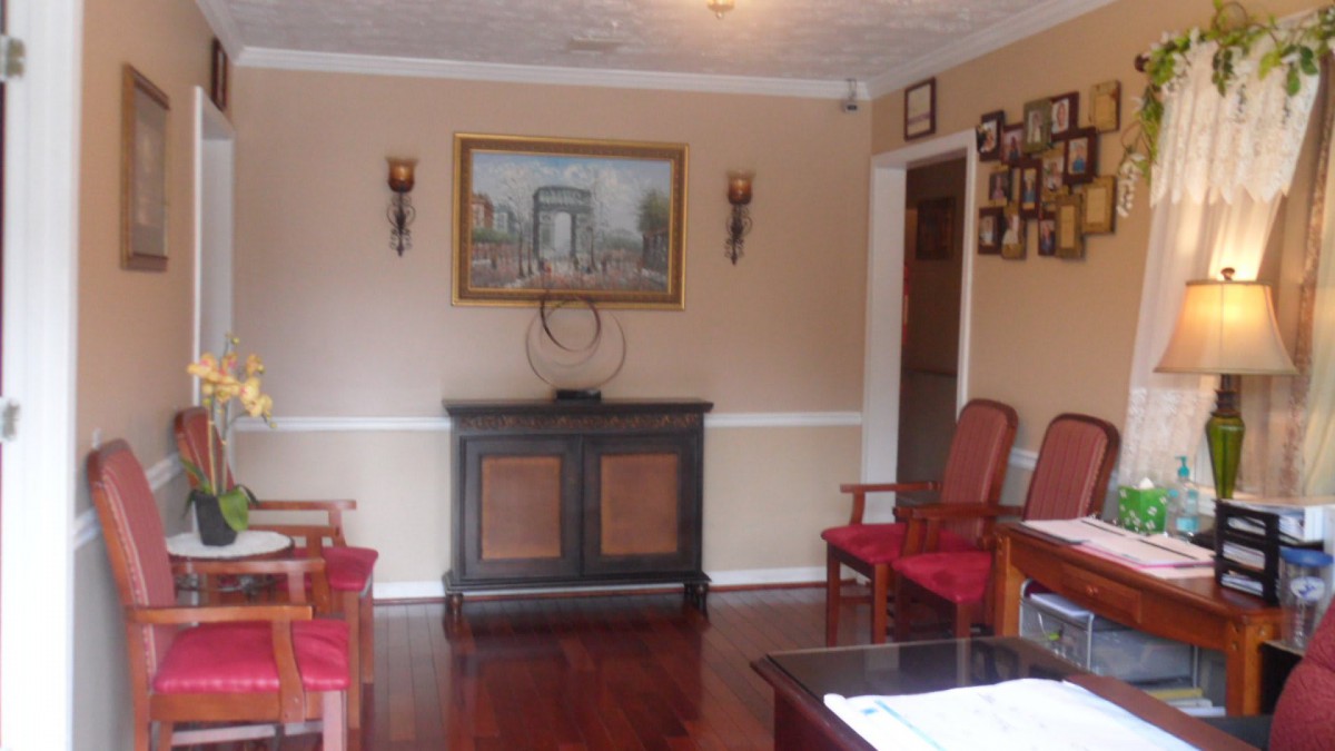 A cozy living room with wooden flooring, featuring a cabinet, red chairs, and a wall painting.