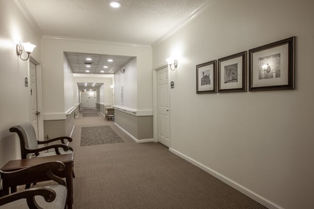 A well-lit hallway with framed pictures on the walls and a carpeted floor.