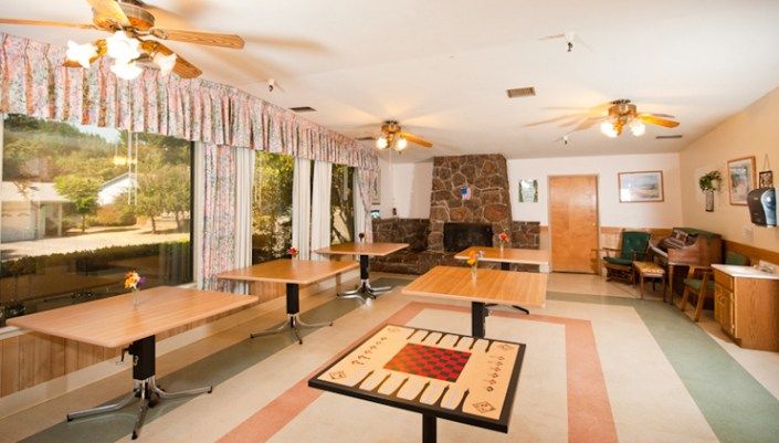 A spacious dining room with several tables and chairs, featuring a fireplace and large windows.