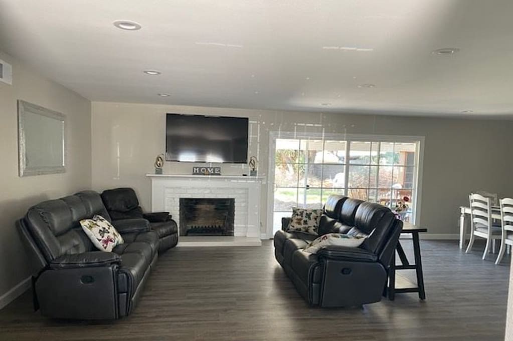 A modern living room with a large television above the fireplace, featuring comfortable sofas and hardwood flooring.
