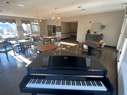 A modern lounge with a piano, featuring tables and chairs bathed in sunlight.