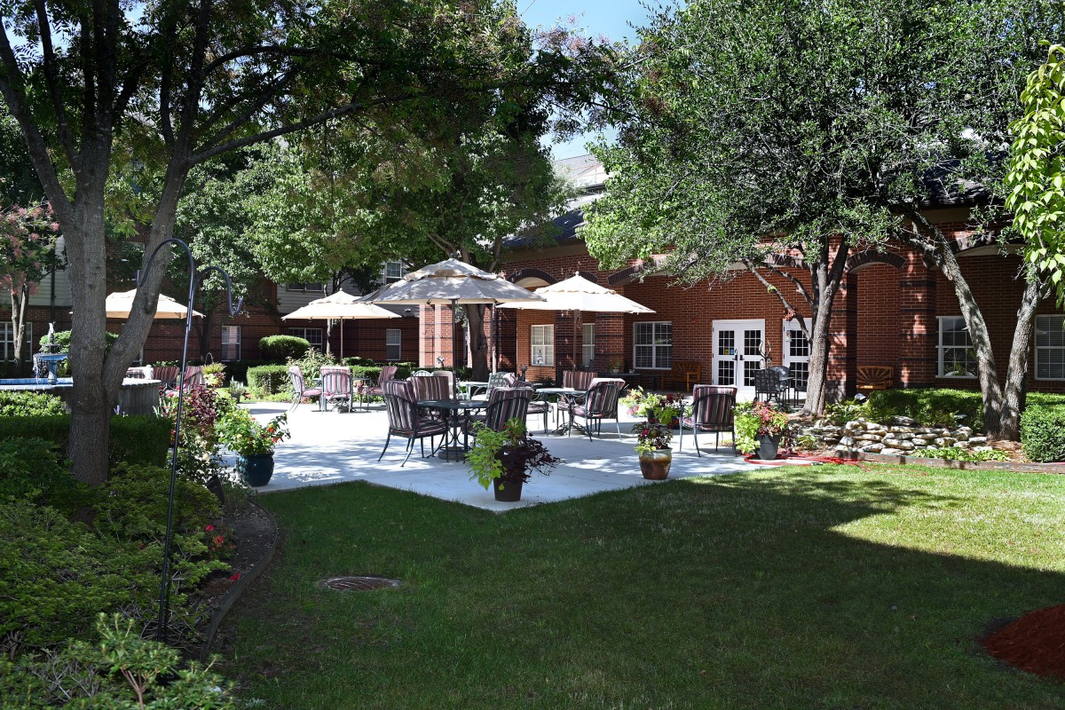 A serene backyard patio with outdoor seating and umbrellas surrounded by lush greenery.