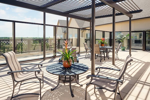 A sunny outdoor patio with tables, chairs, and plants under a pergola.