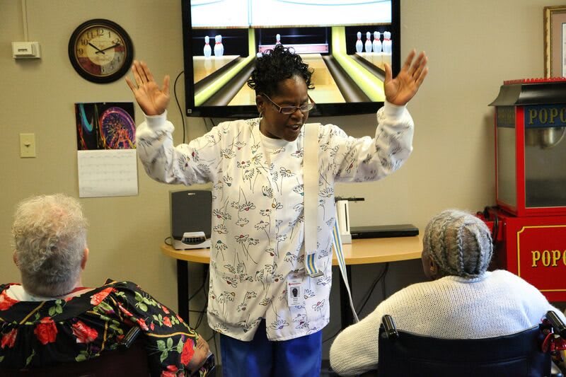 A nurse engages with residents in a recreational activity at a healthcare facility.