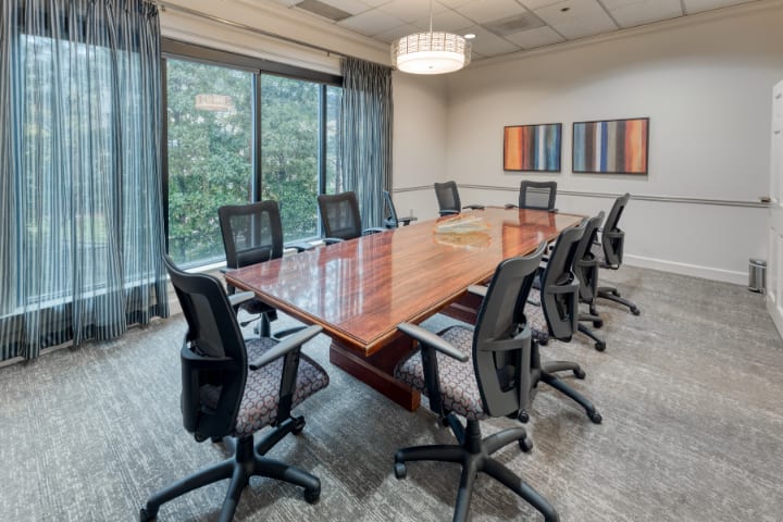 A modern conference room with a large wooden table and ergonomic chairs, featuring large windows and abstract artwork on the walls.