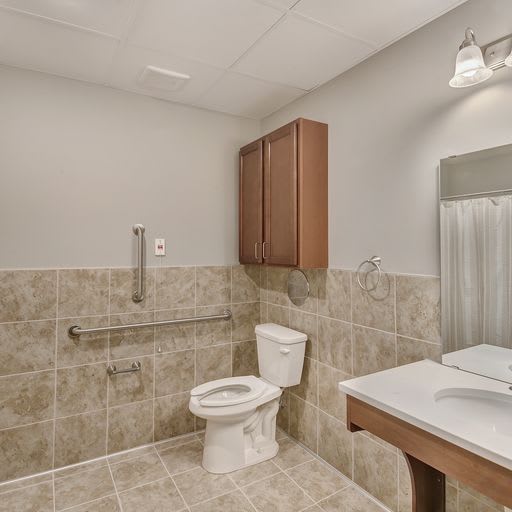 A modern bathroom with tiled walls, featuring a toilet, sink, mirror, and overhead cabinet.