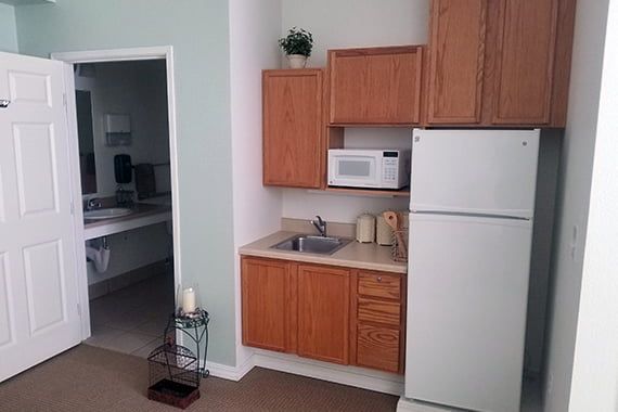 A small apartment kitchen with wooden cabinets, a refrigerator, microwave, and a sink.