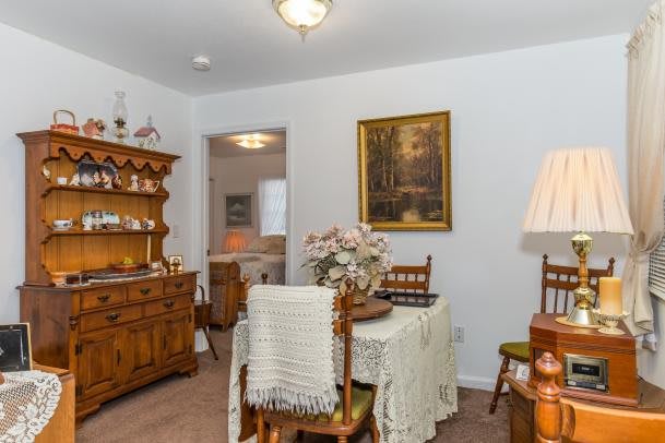 A cozy dining room with vintage wooden furniture, featuring a table set with a lace tablecloth and a hutch displaying decorative items.