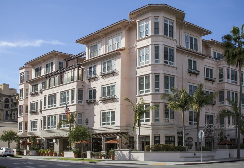 A multi-story residential building with large windows and palm trees in front, viewed from the street.