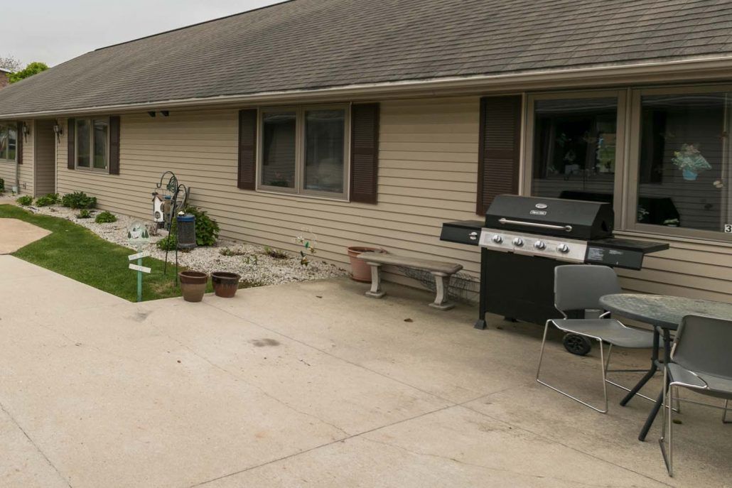 A backyard patio area with a grill, outdoor furniture, and some plants.