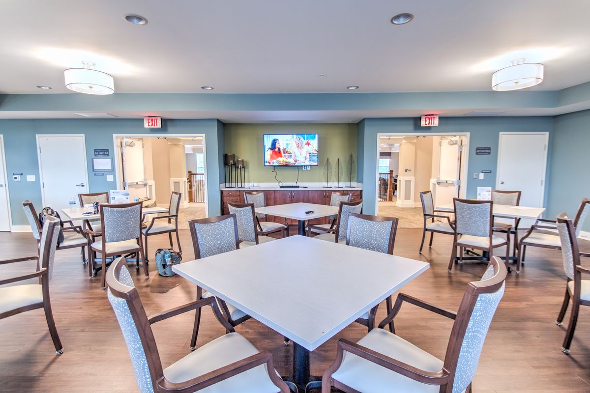 A modern dining area featuring multiple tables and chairs, with a television mounted on the wall, creating a welcoming community space.