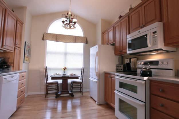 A cozy kitchen with wooden cabinets, modern appliances, and a small dining area with a chandelier.