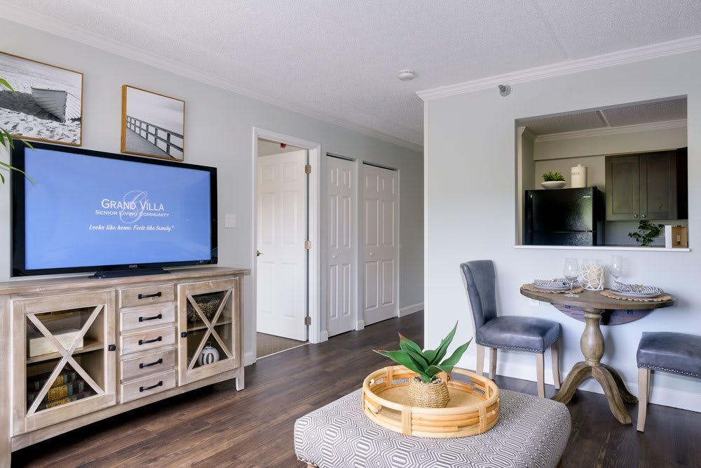 A modern living room with stylish decor, featuring a TV on a wooden stand, a cozy chair and table set, and a decorative plant centerpiece on an ottoman.
