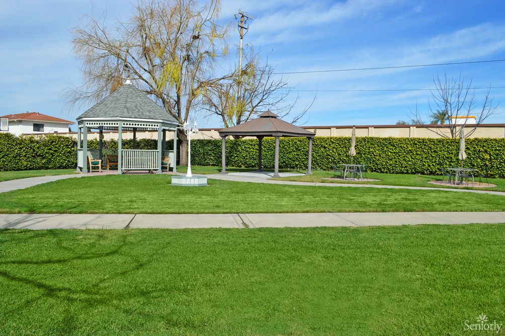 A peaceful park scene with gazebos, lush green lawn, and a clear blue sky.