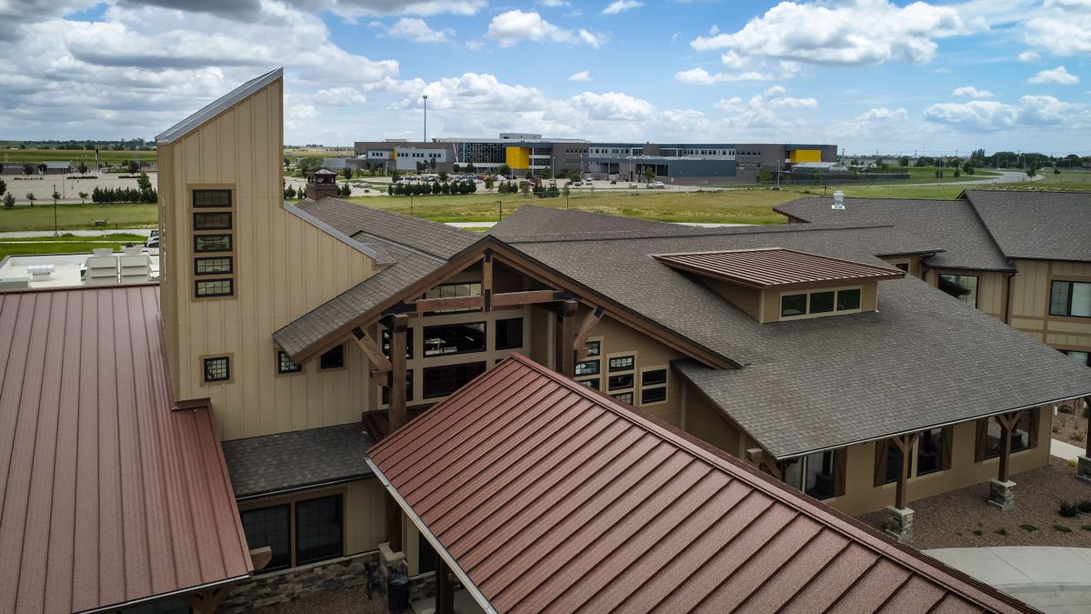 A view of a building with a metal roof and an industrial facility in the background under a partly cloudy sky.