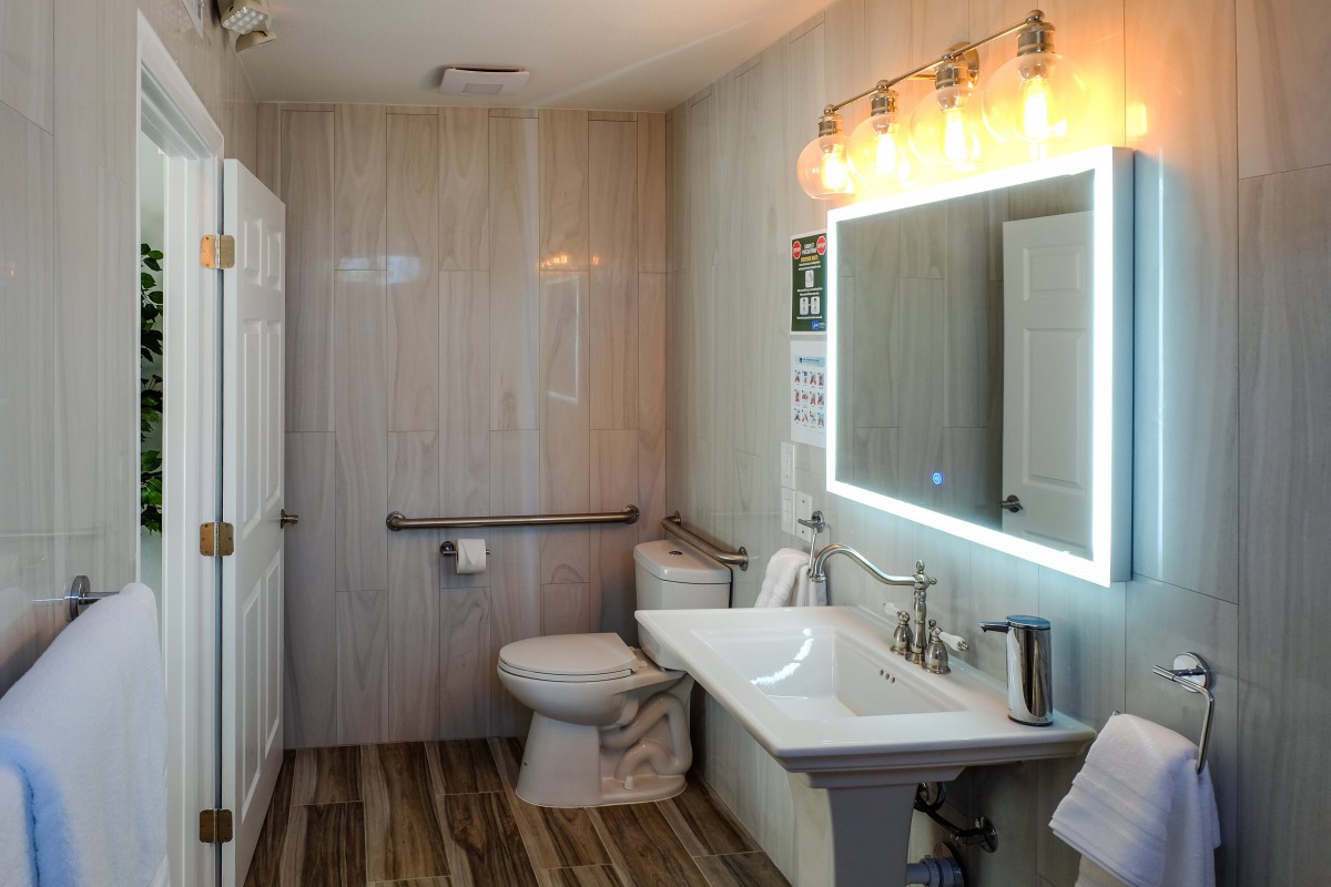 A modern bathroom with a well-lit mirror and wooden flooring.