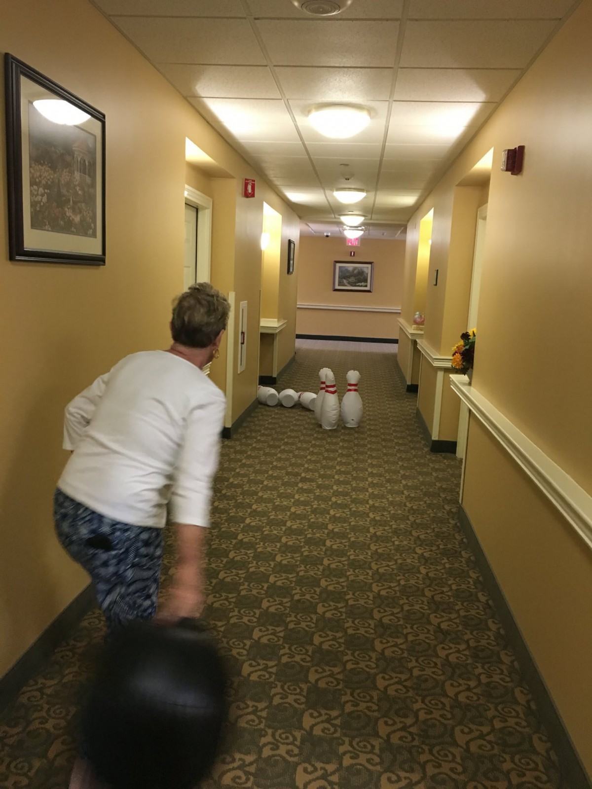 A person bowling in a hallway, aiming at pins set up at the end.