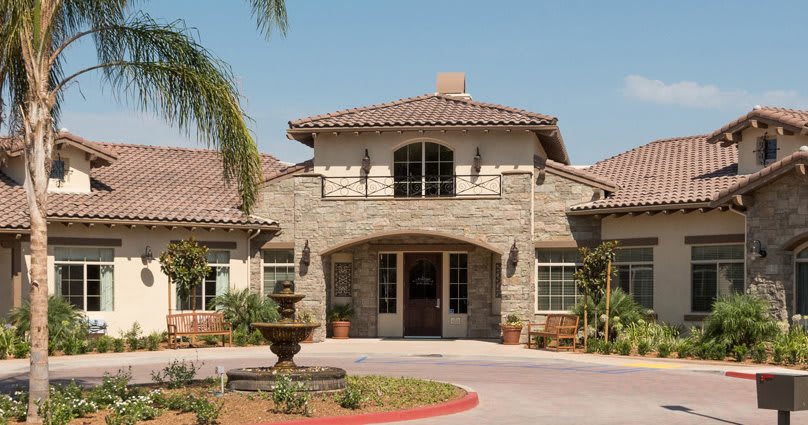 A stone facade residential building with a welcoming entrance, surrounded by palm trees and featuring a fountain in the front.