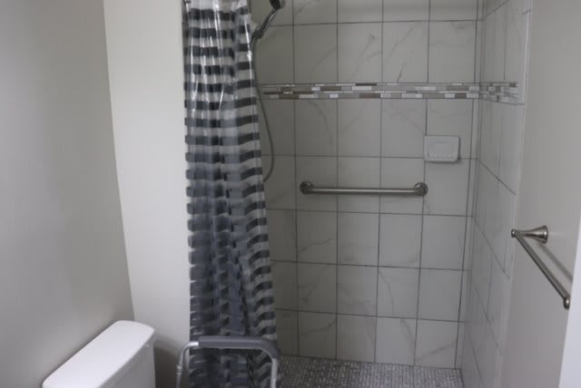 A bathroom featuring a tiled shower with a striped curtain and a grab bar.