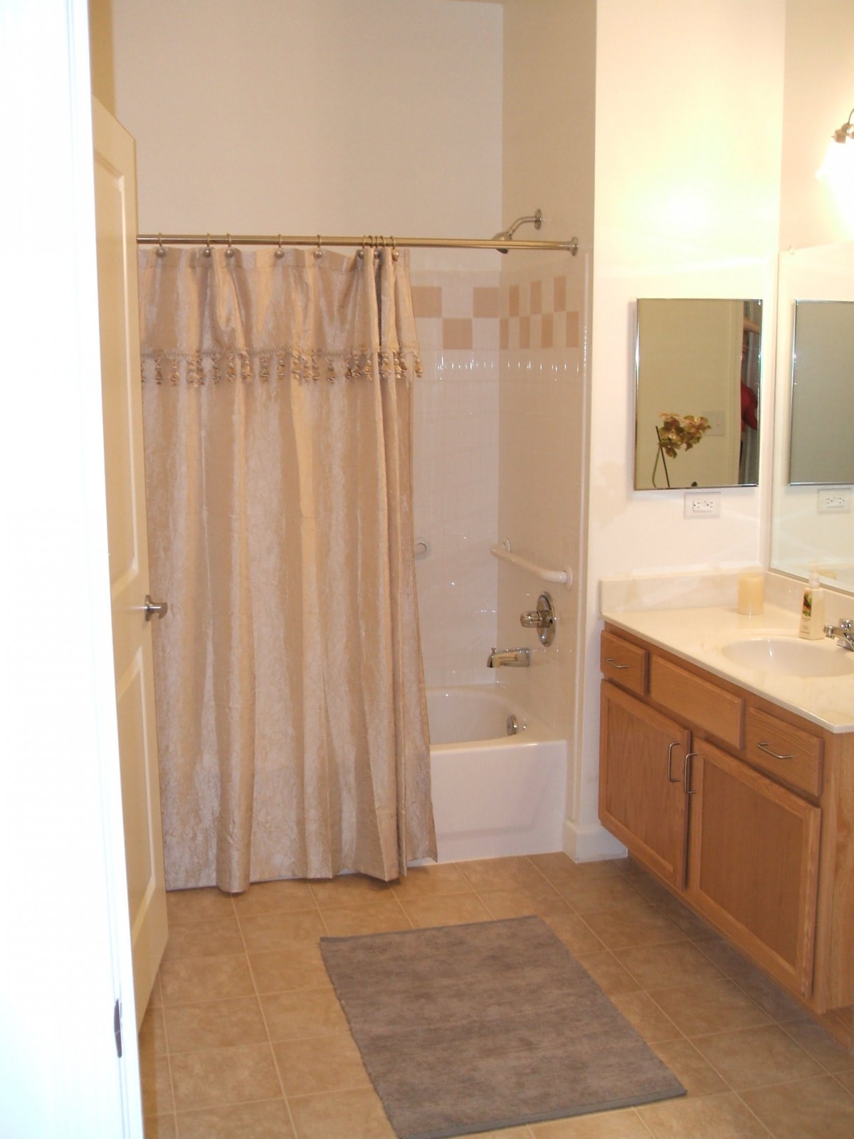 A bathroom with a shower curtain, sink, mirror, and cabinets.