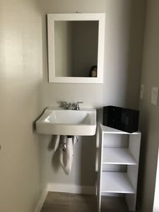 A small bathroom featuring a wall-mounted sink and mirror with adjacent storage shelves.