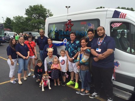 A group of people, including adults and children with a dog, are gathered in front of a decorated van outdoors.