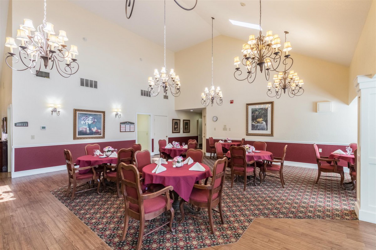 An elegant dining room with chandeliers, red tablecloths, and framed artwork on the walls.