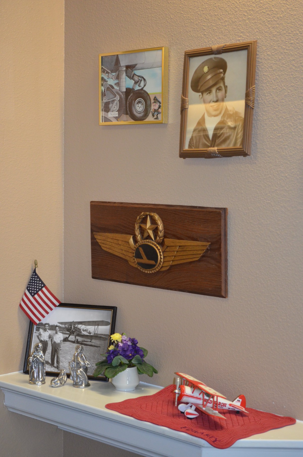 A wall display featuring military memorabilia, including a plaque with wings and a star, photographs, medals, and an American flag.