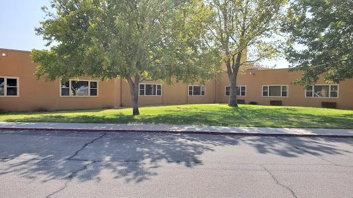 A view of a single-story building surrounded by trees and grass in a sunny environment.