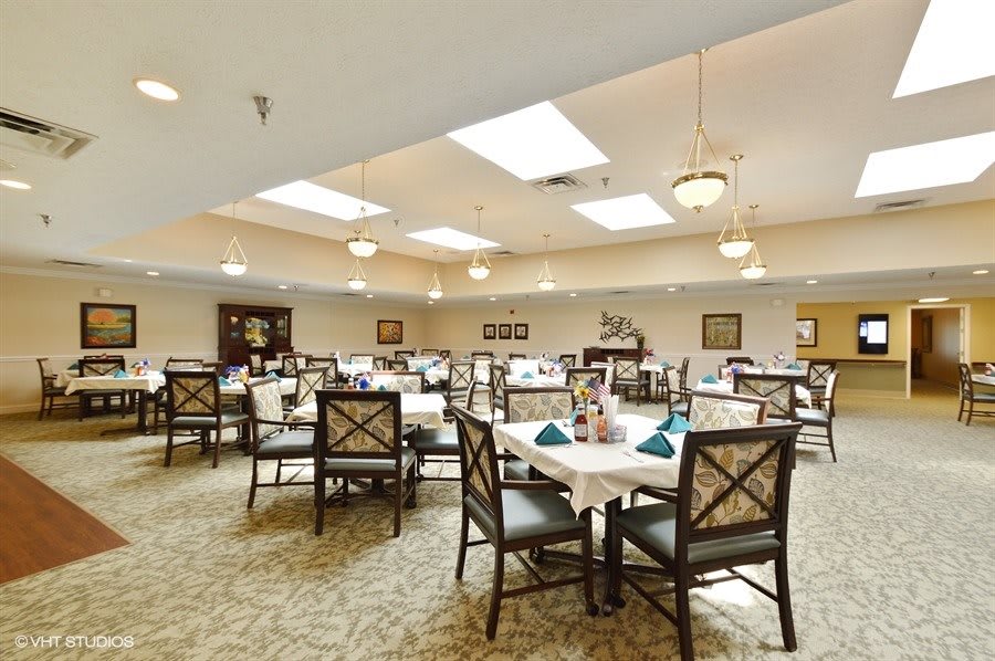 A spacious dining room with neatly arranged tables and chairs, featuring elegant lighting fixtures.
