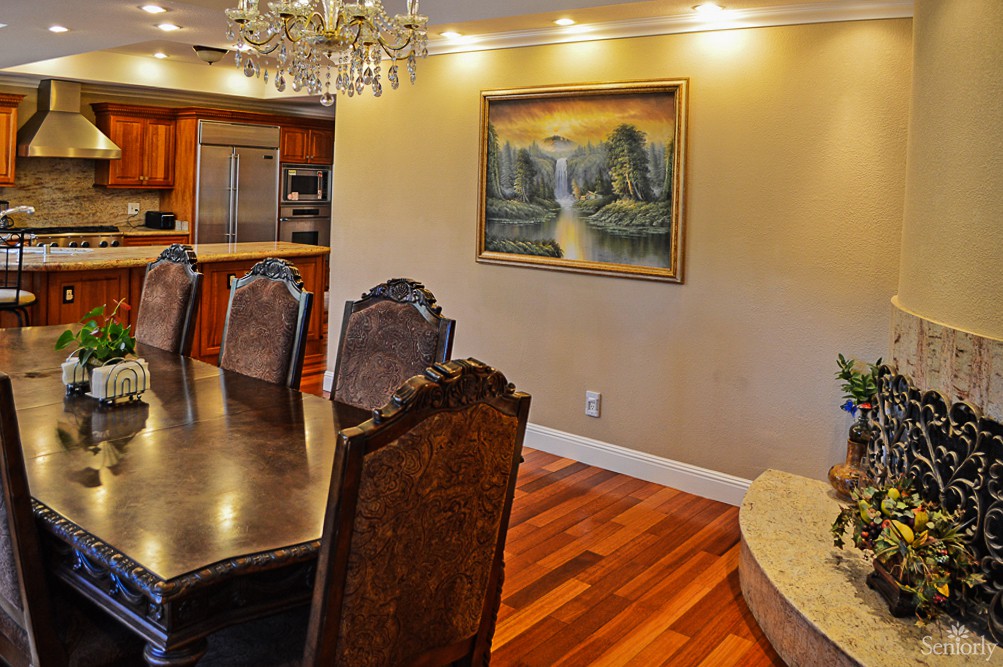 Elegant dining room with a chandelier and a view into the kitchen, featuring wood flooring and a painting on the wall.