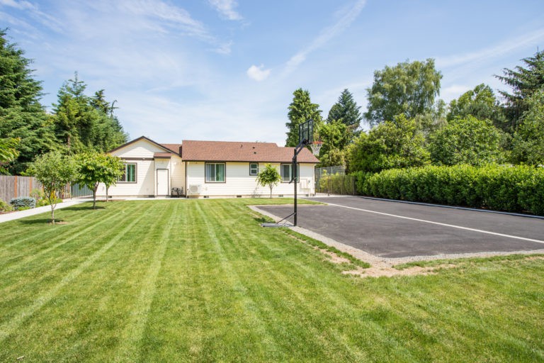 A single-story house with a well-maintained lawn and driveway under a clear sky.