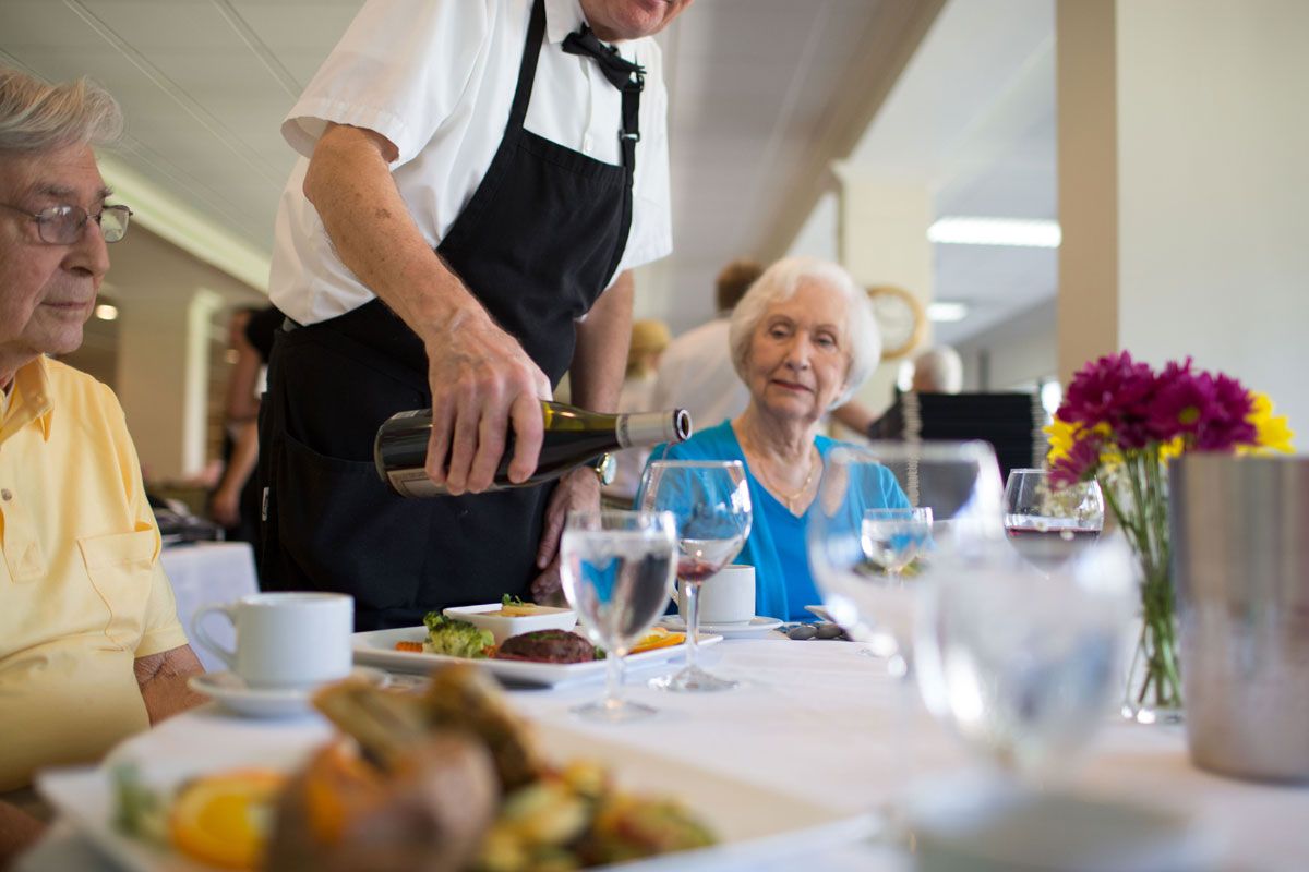 A waiter pours wine for an elderly woman in a restaurant setting.