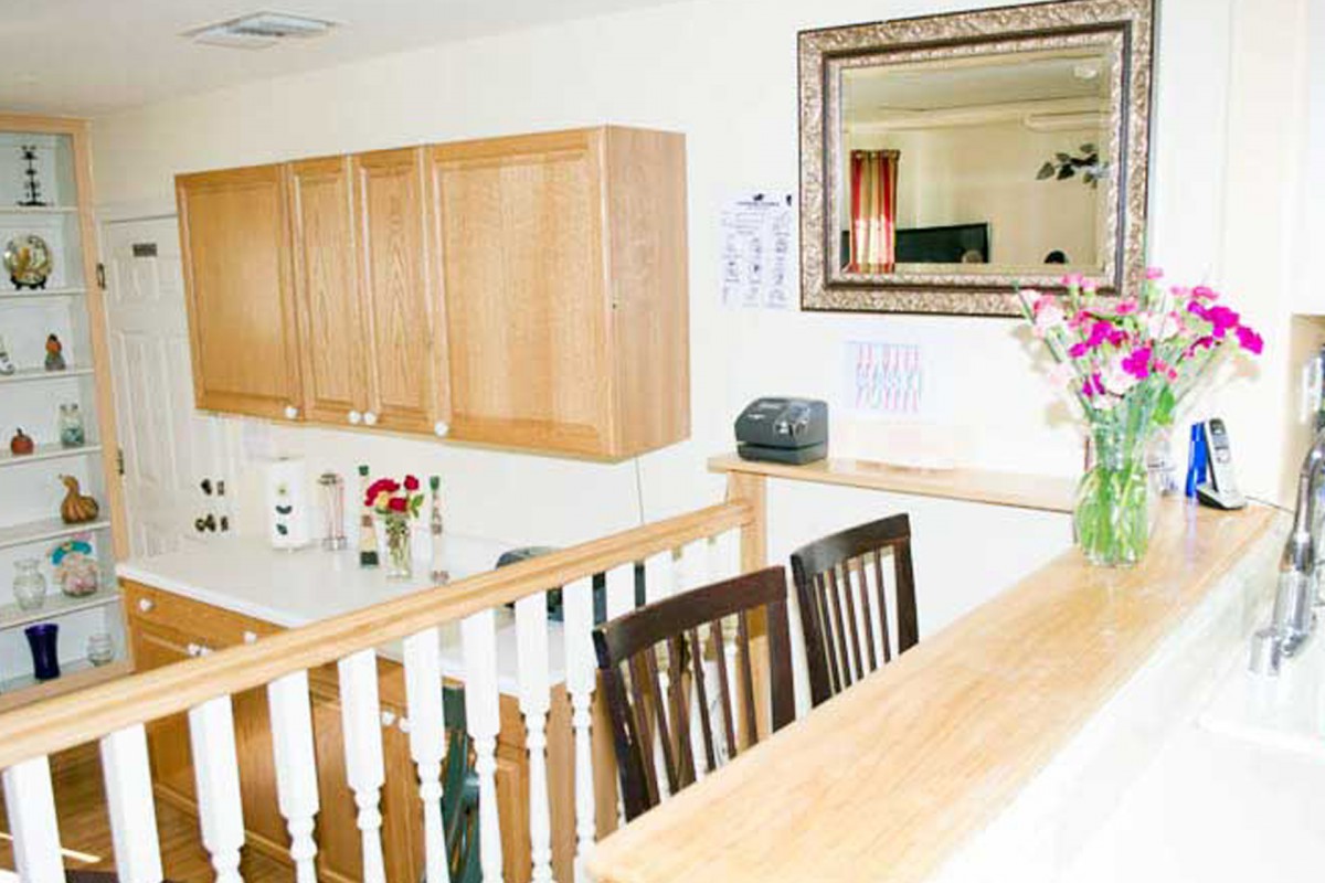 A bright kitchen interior with wooden cabinets, a large mirror, and flowers on the counter.
